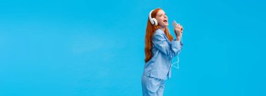 Kız hayalleri yıldız olur. Dikey boy portre çekici ve kaygısız kızıl saçlı genç gece giysisi, donwload karaoke uygulaması, kulaklıkla müzik dinlemek, akıllı telefona şarkı söylemek..