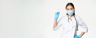 Tıp maskeli Asyalı hemşire elinde aşı şırıngası, sağlık ve aşı konsepti, klinik üniforması, beyaz arka plan..