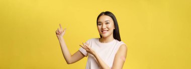 Covid-19 aşı konsepti. Omzunda yama olan gülümseyen Asyalı kız, sağlık afişini işaret ediyor, sarı arka plan.