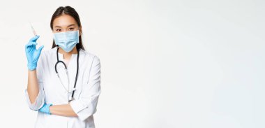 Aşı ve sağlık hizmeti konsepti. Asyalı kadın doktor, tıbbi maske takan hemşire ve aşılı şırınga tutan eldivenler, beyaz arka plan..