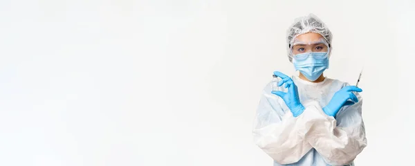 Covid-19 vaccination and health concept. Asian female doctor or nurse in personal protective equipment from coronavirus, showing vaccine covid-19 and syringe, white background.