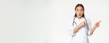 Şaşkın kadın doktor diyor ki vay be, sağı işaret ediyor ve indirimlerle şaşkın şaşkın bakıyor, yolu gösteriyor, beyaz arka plana karşı tıbbi üniforma içinde duruyor..