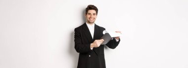 Takım elbiseli kendine güvenen bir işadamının resmi. Belgelere bakıyor, panoya bakıyor ve gülümsüyor..