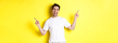 Mutlu stil sahibi adam iki farklı şey gösteriyor. Sol ve sağ tanıtımlarda parmaklarını yana doğru gösteriyor. Sarı arka planda duruyor..