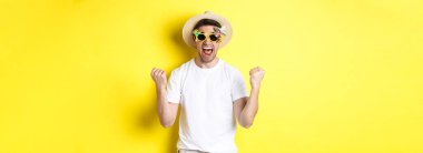 Mutlu adam tatile çıkıyor, kazanıyor ya da kutluyor, yaz şapkası ve güneş gözlüğü takıyor. Turist heyecanlı görünüyor, sarı arka planda duruyor..