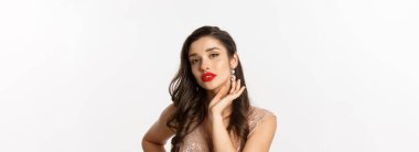 Yeni yıl kutlaması ve kış tatili kavramı. Parti için giyinmiş, lüks küpeler takan, kameraya şehvetli bakan, beyaz arka planı olan güzel bir kadın..