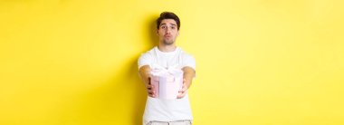 Tatil ve kutlama kavramı. Erkek arkadaş hediye verir ve öpücük için dudaklarını büzer, yıldönümü ya da sevgililer günüyle kutlar, sarı arka plan.