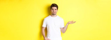 Kafası karışmış ve canı sıkkın adam elini kaldırsın, kafası karışmış, sarı arka plana karşı dursun. Boşluğu kopyala