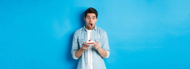 Doğum günü pastasına şaşırmış, mavi arka planda duran bir adam..