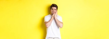 Üzgün adam diş ağrısından şikayetçi, kırlangıç yanağına dokunuyor ve üzgün görünüyor, sarı arka planda duruyor. Boşluğu kopyala