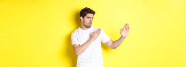 Kung-fu yetenekleri olan bir adam, dövüş sanatları ninja hareketi, beyaz tişörtler içinde dövüşmeye hazır, sarı arka planda duruyor..