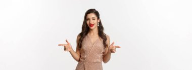 Kutlama, tatil ve parti kavramı. Kırmızı dudaklı, güzel ve çapkın bir kadın. Cazibeli bir elbise giyiyor ve göz kırpıyor. Kamerayı işaret ediyor..