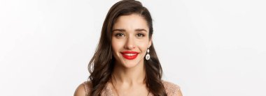 Yeni yıl kutlaması ve kış tatili kavramı. Kırmızı dudaklı güzel bir kadının portresi, lüks küpeler takıyor, kameraya mutlu gülümsüyor, beyaz arka plan.