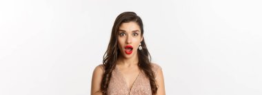 Kırmızı dudaklı, saç stili, elbise giyen, kameraya şaşırmış beyaz arka planda duran çekici bir kadın..