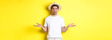 Turizm ve yaz kavramı. Kafası karışmış gezgin omuz silkiyor, bir şey anlayamıyor, sarı arka planda duruyor..