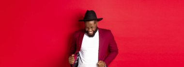 Noel ve insanlar kavramı. Mutlu siyah adam yeni yılı kutluyor ve dans ediyor, parti kıyafeti giyiyor, kırmızı arka plan.