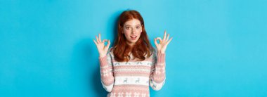 Kendine güveni tam kızıl saçlı bir kadının görüntüsü. Her şeyin yolunda olduğuna emin, övgüyle seçilmiş, mavi arka planda duruyor..