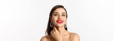 Moda ve güzellik konsepti. Kırmızı dudakları olan, yüzüne dokunan, kendinden emin gülümseyen, beyaz arka planda duran muhteşem esmer kadının yakın çekimi..