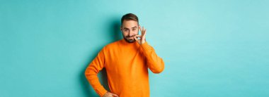 Yakışıklı sakallı adam söz veriyor ağzını kapalı tut, dudaklarını mühürle, ağzını kilitle, açık mavi arka planda dur..