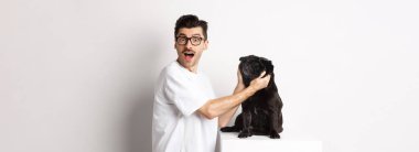 Mutlu genç adam sana köpeğinin sevimli yüzünü gösteriyor. Köpek sahibi hayvanını seviyor, beyaz arka planda duruyor..