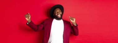 Noel ve insanlar kavramı. Mutlu siyah adam yeni yılı kutluyor ve dans ediyor, parti kıyafeti giyiyor, kırmızı arka plan.