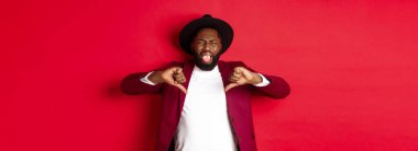 Noel alışverişi ve insanların konsepti. Siyahi adamın dil göstermesi iğrençtir. Kötü bir şeyden hoşlanmaz, kötü bir ürünü yargılar, kırmızı arka plan..