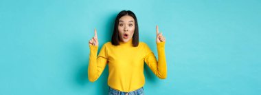 Alışveriş konsepti. Etkilenmiş genç Koreli kadın üzerinde reklam gösteriyor, parmaklarını havaya kaldırıyor ve hayrete düşüyor, 