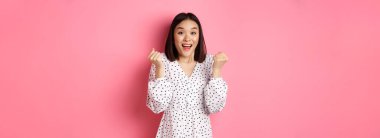 Asyalı güzel bir kadının kazandığını, yumruklarını sıktığını ve mutlu bir yüzle evet dediğini zafer kazandığını ve pembe arka planda dikildiğini hayal et..