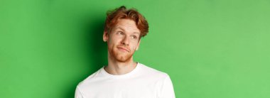 Saçları dağınık ve sakallı, gülümseyen kızıl saçlı adam, mutlu bir yüzle sola bakıyor, yeşil arka planda duruyor..