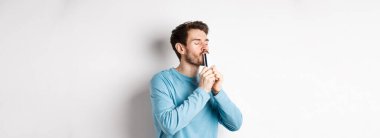 Plastik kredi kartını öpen genç adam, tatmin olmuş bir yüzle beyaz arka planda dikiliyor, mavi gömlekli..