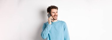 Teknoloji konsepti. Neşeli adam telefonla konuşmaktan hoşlanıyor, akıllı telefondan konuşuyor ve gülümsüyor, beyaz arka planda sıradan bir tişörtle dikiliyor..