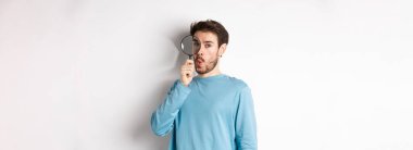 Şaşırmış bir adam bir şey buldu. Büyüteçten bakıp şaşkın şaşkın baktı. Beyaz arka planda duruyordu..