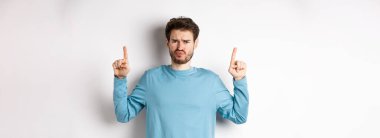 Hayal kırıklığına uğramış erkek model somurtuyor, olumsuz duygularla parmakla işaret ediyor, tanıtım teklifinden hoşlanmıyor, beyaz arka planda duruyor..