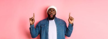 Hayal kırıklığına uğramış Afrikalı Amerikalı adam şikayet ediyor, kötü tanıtıma bakıyor ve işaret ediyor, pembe arka plana karşı hoşnutsuz duruyor..