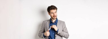 Kendine güveni tam ve başarılı bir iş adamı gibi görünen ve beyaz arka planda duran plastik kredi kartını takım elbisenin cebine koyan..