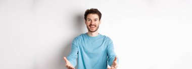 Gündelik giysiler içindeki çekici beyaz adam bir şeyi tutmak için ellerini uzatıyor, gülümsüyor ve alıyor, beyaz arka planda duruyor..