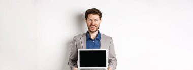 Takım elbiseli yakışıklı beyaz işadamı boş laptop ekranı gösteriyor, tanıtım yapıyor, beyaz arka planda duruyor..