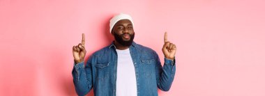 Memnun yakışıklı siyahi adam onaylamak için başını sallıyor ve iyi bir tanıtıma bakıyor, teklifini işaret ediyor, en iyisini gösteriyor, pembe arka plan..