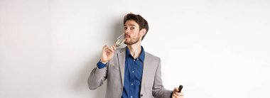 Kutlama ve tatil konsepti. Yakışıklı, sakallı, takım elbiseli, elinde şapka şişesi olan, bir bardak şampanya içen, beyaz arka planda duran....