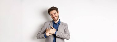 Takım elbiseli mutlu adam kalbe sarılmış, dokunulmuş ya da minnettar hissediyor, ruhunda yumuşak anılara sahip, beyaz arka planda duruyor..