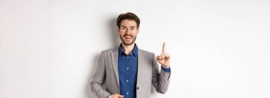 Heyecanlı takım elbiseli işadamı iyi fikir sunuyor, Eureka işaretinde parmağını kaldırıyor ve komik görünüyor, öneriler söylüyor, beyaz arka planda duruyor..