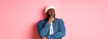 Düşünceli Afro-Amerikan erkek model karar veriyor, endişeli görünüyor, düşünüyor ya da şüphe duyuyor, pembe arka planda duruyor..