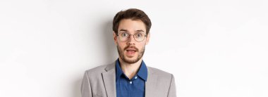 Gözlüklü ve takım elbiseli şaşkın iş adamının yakın çekimi hayret içinde, iyi haberleri duy, beyaz arka planda dur..