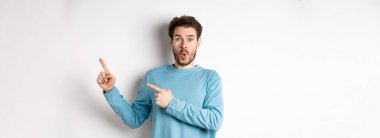 Vay canına, şuna bak. Etkilenmiş genç adam parmaklarını sağa gösteriyor ve logoyu gösteriyor, beyaz arka planda şaşkın şaşkın duruyor..