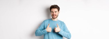 İyi seçim. Çekici beyaz sakallı adam başparmağını kaldırıyor ve gülümsüyor, iyi bir ürünü onaylıyor ve onaylıyor, bir şeyler öneriyor, beyaz arka planda duruyor..