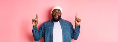 Mutlu Afro-Amerikan adam reklamını yapıyor, şaşırmış bir şekilde gülümsüyor ve kameraya bakıyor, parmaklarını havaya kaldırıyor, pembe arka plan.