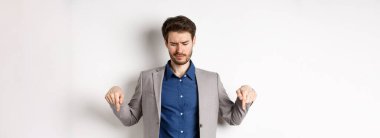 Etkilenmemiş genç işadamı hayal kırıklığına uğradı, kötü terfiyi işaret etti ve hor gördü, beyaz arka planda hoşnutsuzdu..