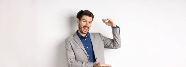 Takım elbiseli yakışıklı bir satıcı, büyük gelir elde ediyor, kameraya hevesle gülümsüyor, beyaz arka planda duruyor..