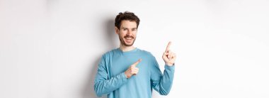 Fotokopi alanında reklam gösteren neşeli sakallı adam sol üst köşedeki logoyu işaret ediyor ve gülümsüyor, beyaz arka planın üzerinde duruyor..