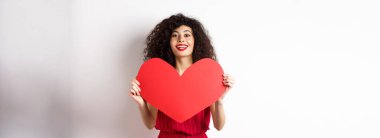 Büyük kırmızı kalp gösteren romantik bir kadın, aşık oluyor, kameraya mutlu bir şekilde gülümsüyor, beyaz arka plan.